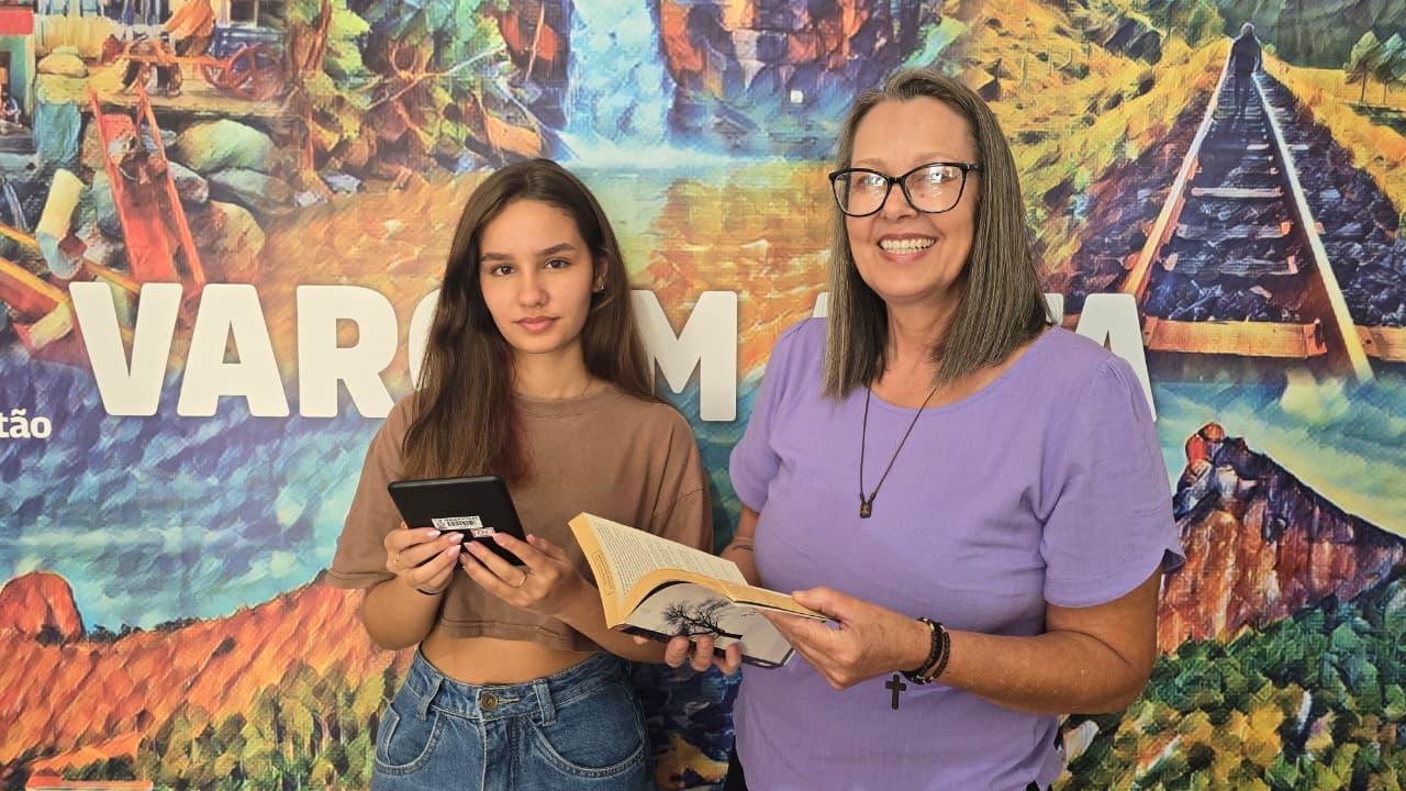 A estudante Theodora Marchetti, com um Kindle, e a bibliotecária Andreia Marchetti, com um livro do acervo, representam a integração entre a leitura digital e a tradicional nas bibliotecas públicas de Vargem Alta. 📸 Foto: Cláudio Pazetto